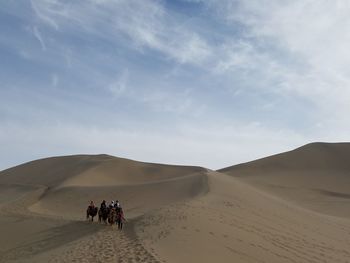 People on sand dune in desert against sky