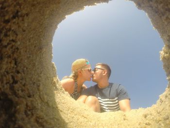 Young couple kissing against sky seen through sand