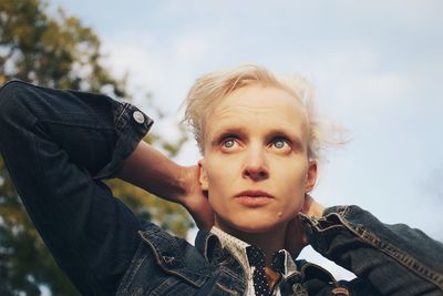 Woman with hand in hair looking away against trees and sky