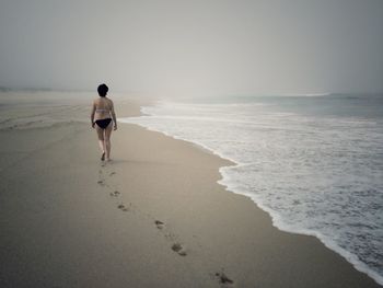 Rear view of woman walking on shore at beach
