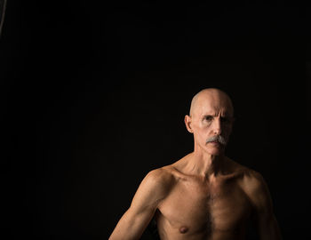 Portrait of mature man with shaved head against black background