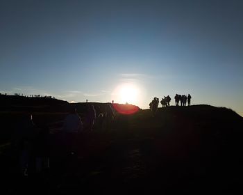 Silhouette people on land against sky during sunset