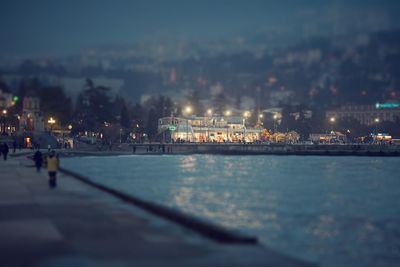 Illuminated city by sea against sky at night