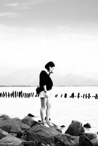Full length of woman standing on rock at seashore against sky