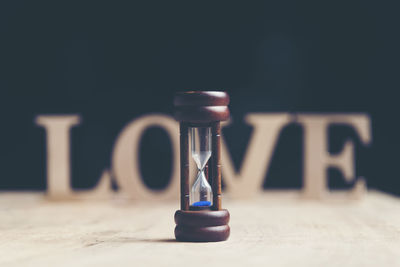 Close-up of hourglass with love text on table against black background