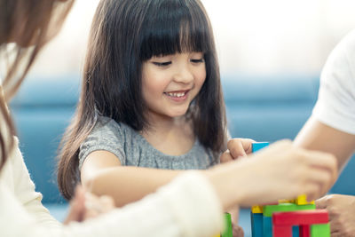 Smiling girl and parents playing with toy blocks in living room at home