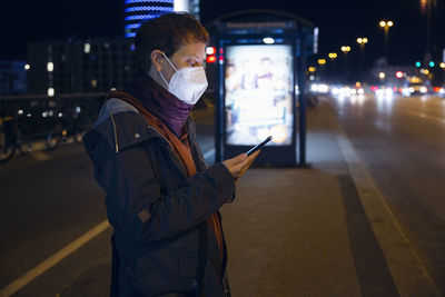 Man using mobile phone while standing on street at night