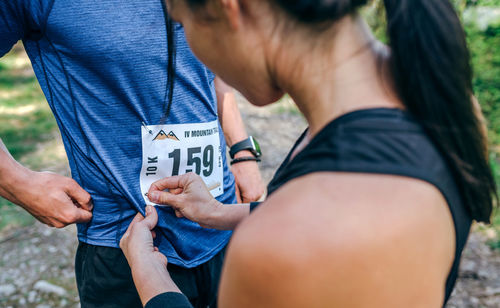 Midsection of man attaching marathon bib while standing in forest