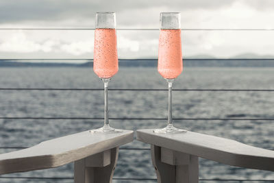 Champagne flutes on table at seaside against cloudy sky