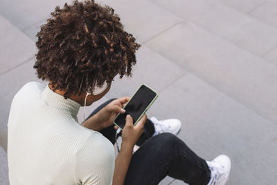 Young curly woman typing a text message through her smartphone, latin teen 