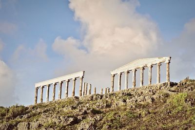 Low angle view of old ruins on mountain against cloudy sky during sunny day