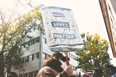 Low angle portrait of woman holding text against trees in city