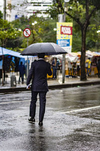 Full length of man walking on wet street during rainy season