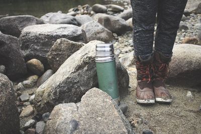 Low section of woman standing by insulated drink container on rocks