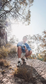 Young man sitting on land against trees