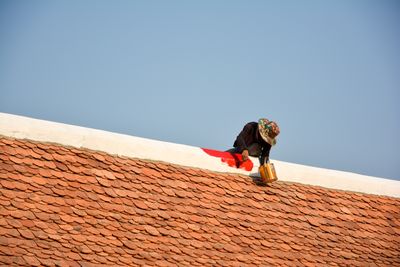 Low angle view of person on roof against clear blue sky