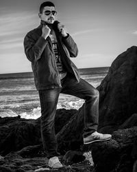 Portrait of man on rock at sea shore against sky