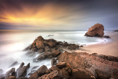 Rocks on beach against sky during sunset