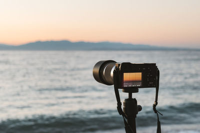 Vintage camera at beach against clear sky during sunset