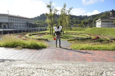 Rear view of man wearing costume wing standing at park by building