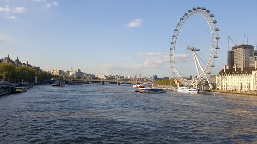 Ferris wheel by river against sky in city