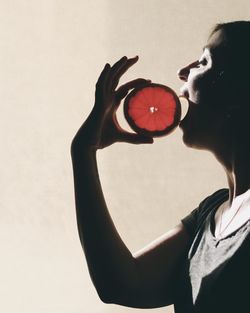 Side view of woman eating citrus fruit by wall
