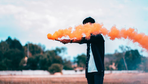 Man holding umbrella against orange sky