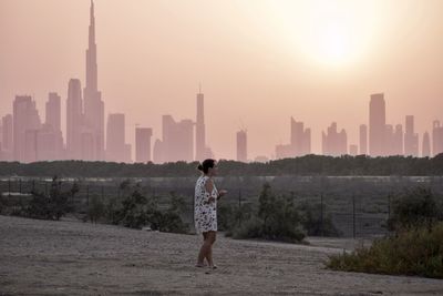 Full length of woman standing against buildings in city sunset