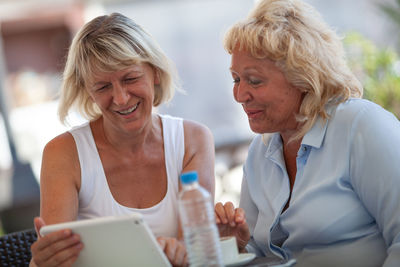 Mature woman showing digital tablet to friend at sidewalk cafe