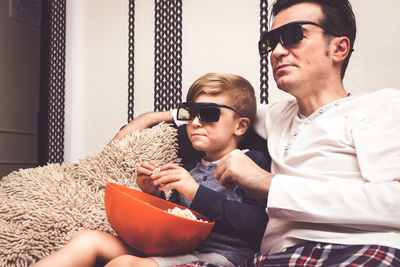 Father and son eating popcorn while watching movie at home