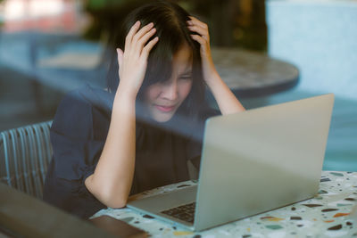 Woman with head in hands wearing while mask sitting by laptop on table