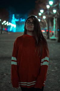 Young woman standing against illuminated wall at night