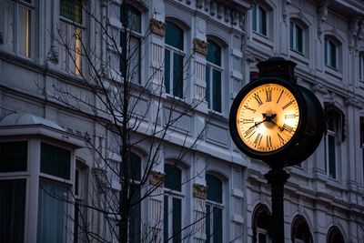 Low angle view of illuminated clock against building at dusk