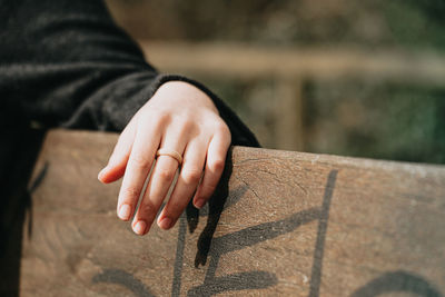 Cropped image of woman wearing ring sitting on bench outdoors