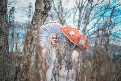 Woman standing by bare trees in forest