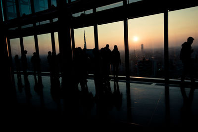 Silhouette people standing by window in city during sunset