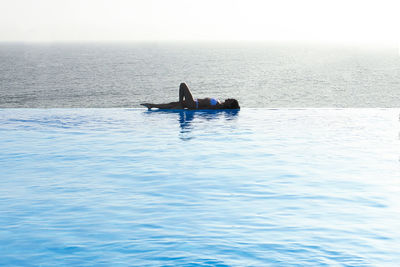 Woman lying amidst swimming pool and sea