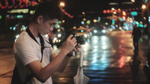 Side view of young man photographing in city at night