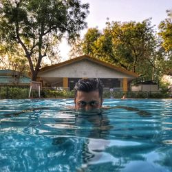 Portrait of man swimming in pool against trees