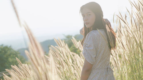 Portrait of young woman standing on field against sky