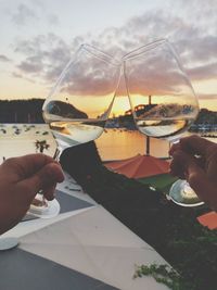 Close-up of hand holding wine glass against sky