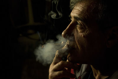 Close-up of man smoking against black background