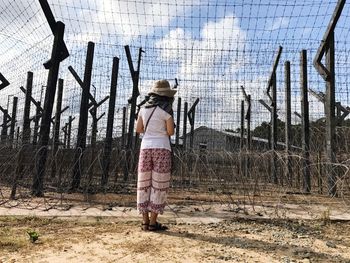 Rear view of woman standing on field by fence