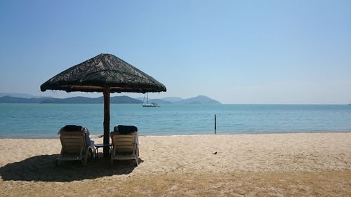 Chair on beach by sea against clear sky