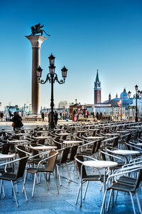 Chairs and tables arranged at sidewalk cafe against clear blue sky in city