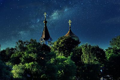 Low angle view of cross amidst trees against sky at night