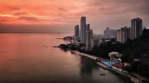 Sea by buildings against sky during sunset
