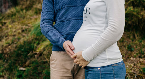 Midsection of pregnant woman standing with man on field
