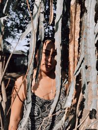 Portrait of young woman standing by tree trunk