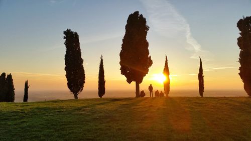 Silhouette people on landscape against sky during sunset